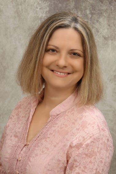 Focused African American female teacher in formal clothes standing near school desk with diverse pupils and pointing at schoolboys copybook